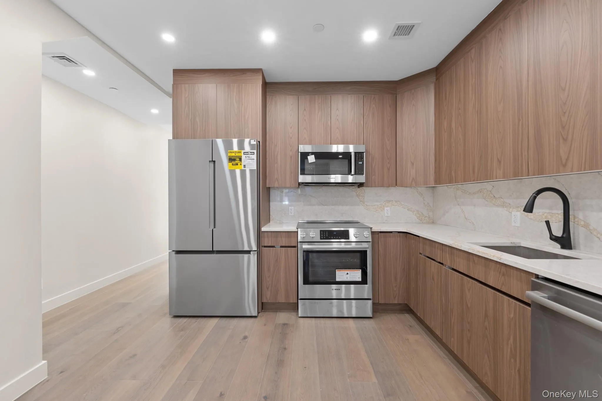 Kitchen with light stone counters, modern cabinets, stainless steel appliances, recessed lighting, and light wood finished floors Kitchen with light stone counters, modern cabinets, stainless steel appliances, recessed lighting, and light wood finished floors