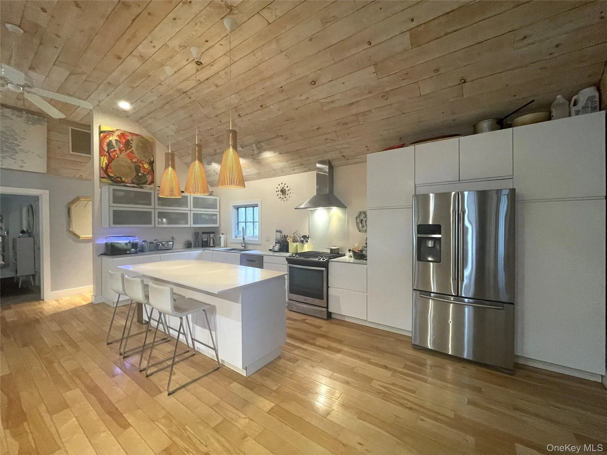 Kitchen featuring appliances with stainless steel finishes, a breakfast bar area, white cabinets, hanging light fixtures, and wall chimney range hood