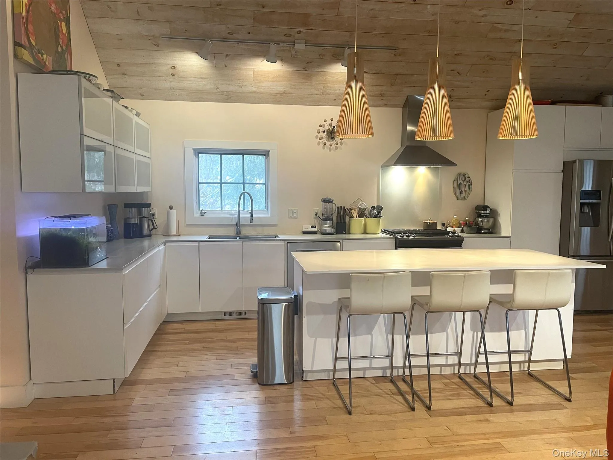 Kitchen featuring a kitchen breakfast bar, appliances with stainless steel finishes, wall chimney exhaust hood, white cabinetry, and light countertops