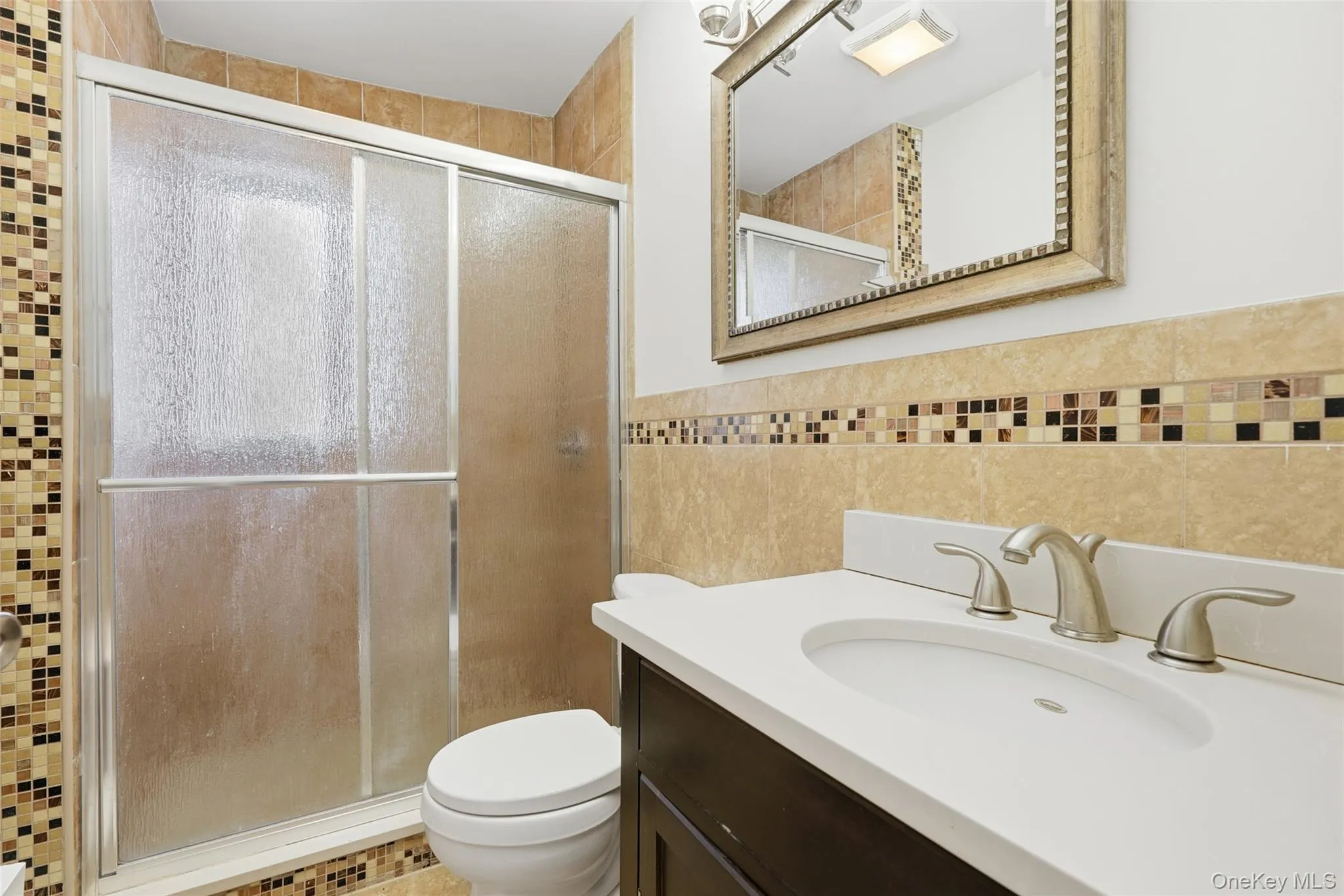 Full bath with vanity, tile walls, a stall shower, and wainscoting Full bath with vanity, tile walls, a stall shower, and wainscoting