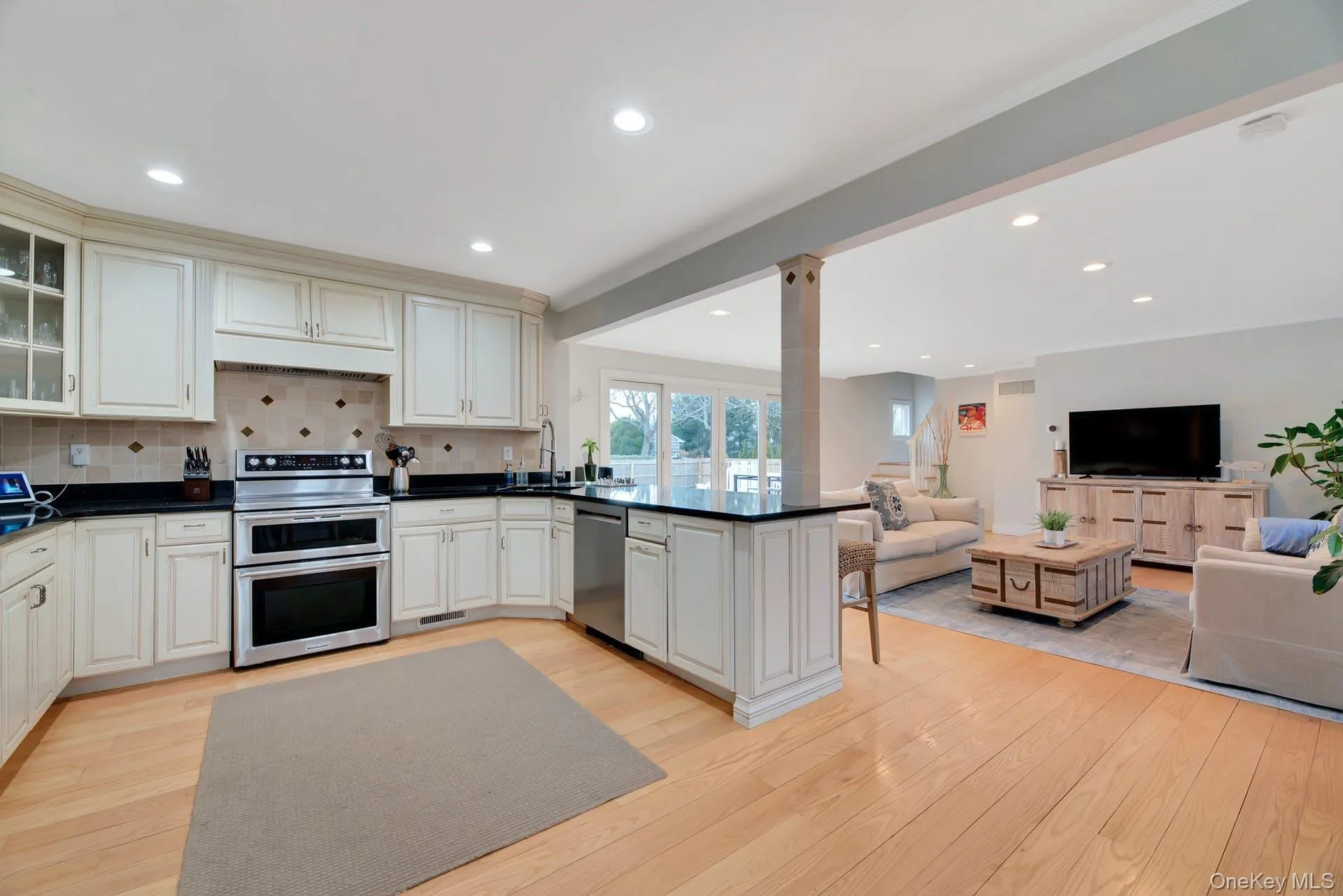 Kitchen featuring stainless steel appliances, open floor plan, glass insert cabinets, a peninsula, and light wood finished floors Kitchen featuring stainless steel appliances, open floor plan, glass insert cabinets, a peninsula, and light wood finished floors