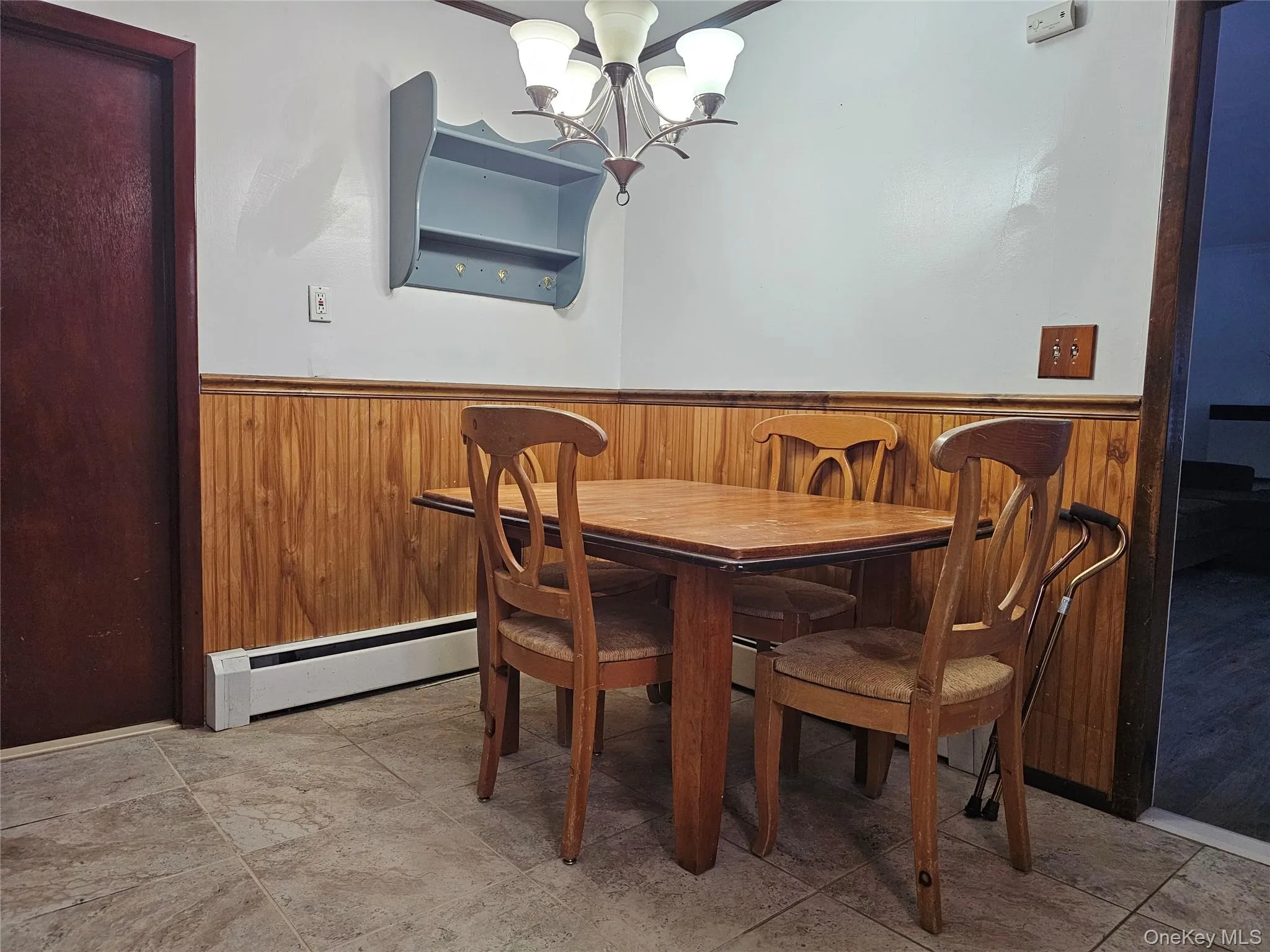 Dining room with a wainscoted wall, wooden walls, a chandelier, and baseboard heating Dining room with a wainscoted wall, wooden walls, a chandelier, and baseboard heating