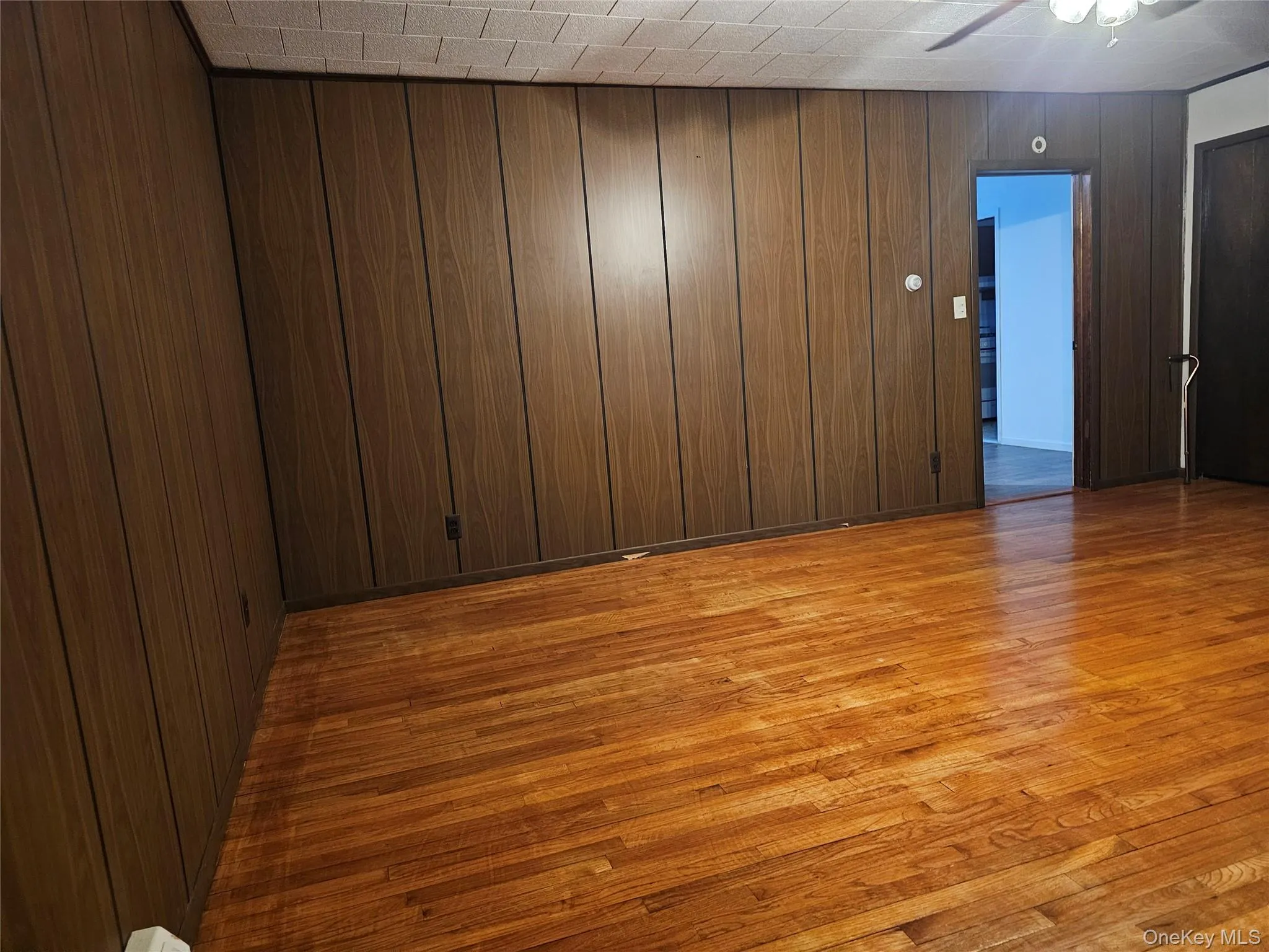 Empty room featuring light wood finished floors, wood walls, and ceiling fan Empty room featuring light wood finished floors, wood walls, and ceiling fan