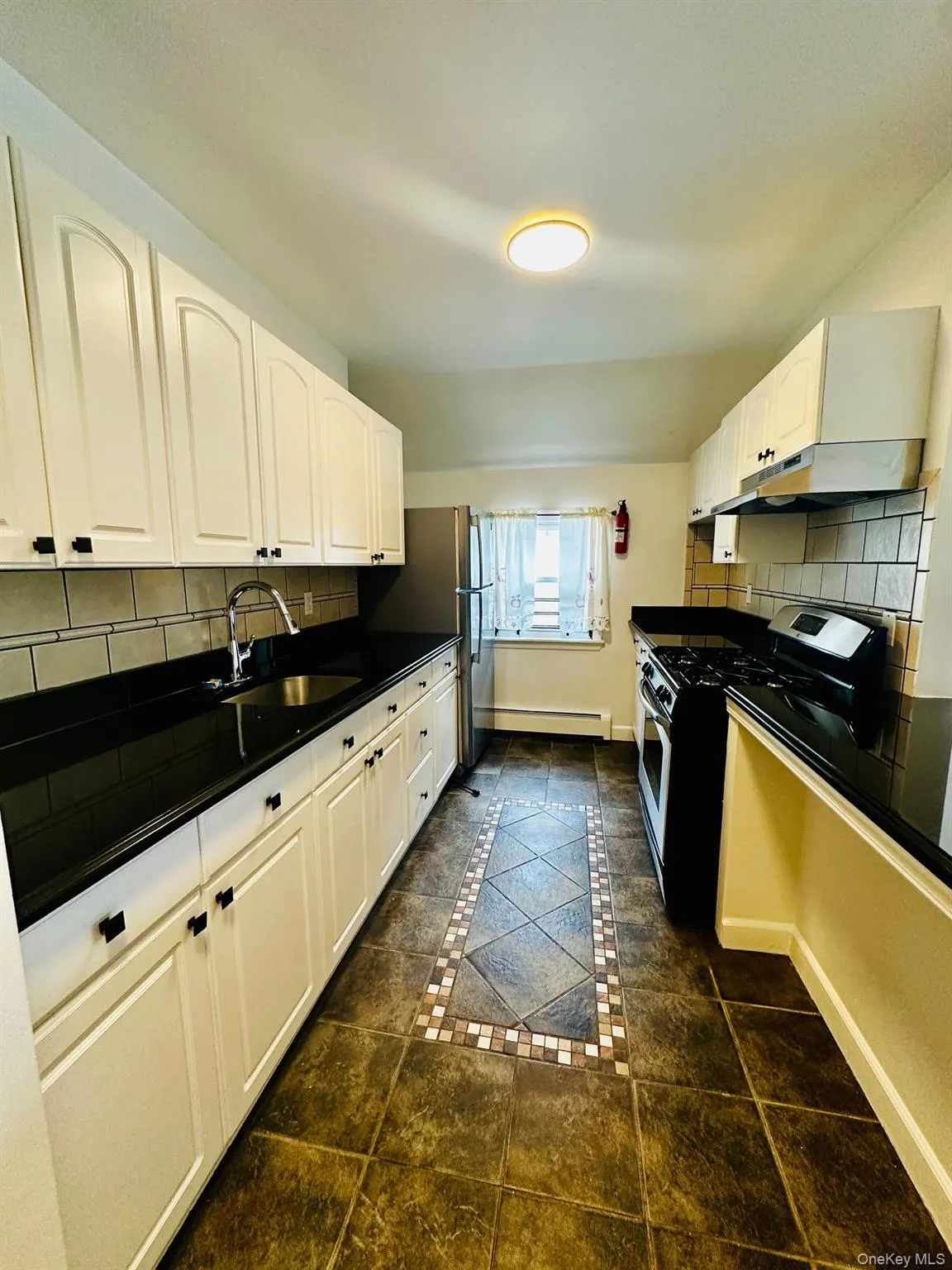 Kitchen with backsplash, inlaid floor details, stainless steel appliances, and white cabinets Kitchen with backsplash, inlaid floor details, stainless steel appliances, and white cabinets