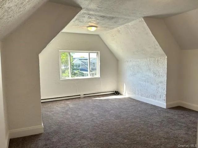Bonus room featuring a textured ceiling, a textured wall, lofted ceiling, carpet flooring, and baseboard heating Bonus room featuring a textured ceiling, a textured wall, lofted ceiling, carpet flooring, and baseboard heating