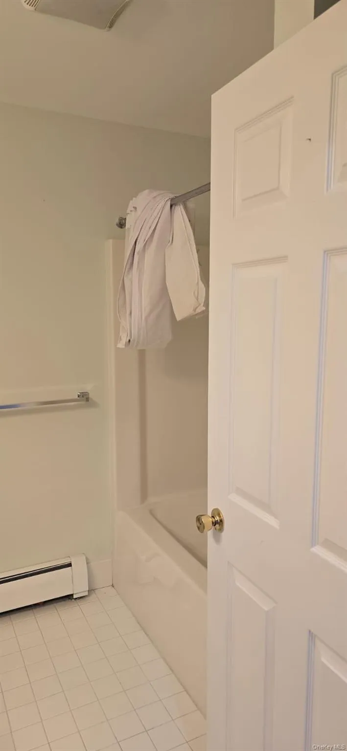 Bathroom featuring baseboard heating, light tile patterned floors, a tub, and a shower Bathroom featuring baseboard heating, light tile patterned floors, a tub, and a shower