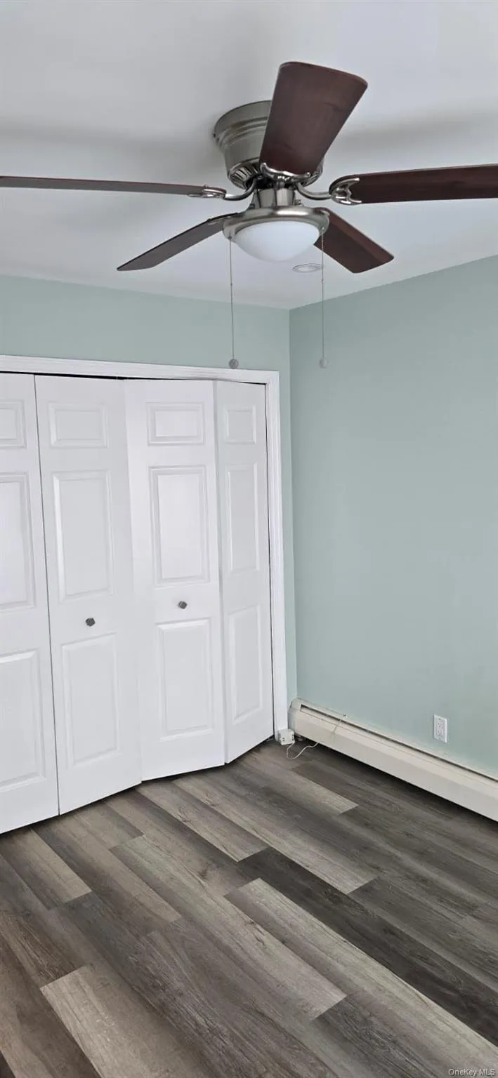 Unfurnished bedroom with baseboard heating, dark wood-style floors, ceiling fan, and a closet Unfurnished bedroom with baseboard heating, dark wood-style floors, ceiling fan, and a closet