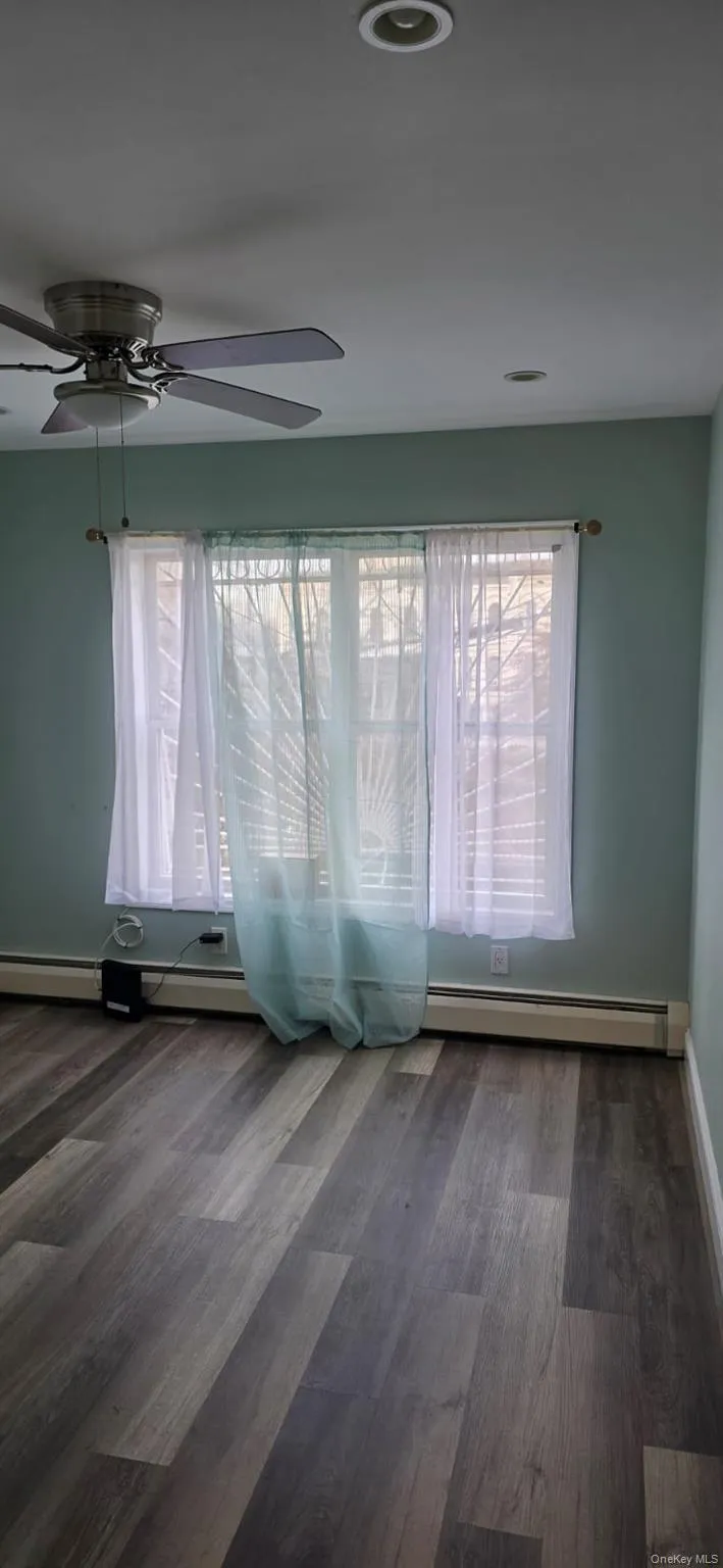 Empty room featuring ceiling fan, dark wood-style floors, and a baseboard radiator Empty room featuring ceiling fan, dark wood-style floors, and a baseboard radiator
