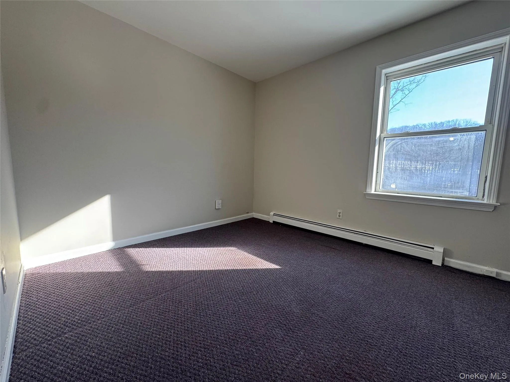 Unfurnished room with a baseboard heating unit and dark carpet Unfurnished room with a baseboard heating unit and dark carpet