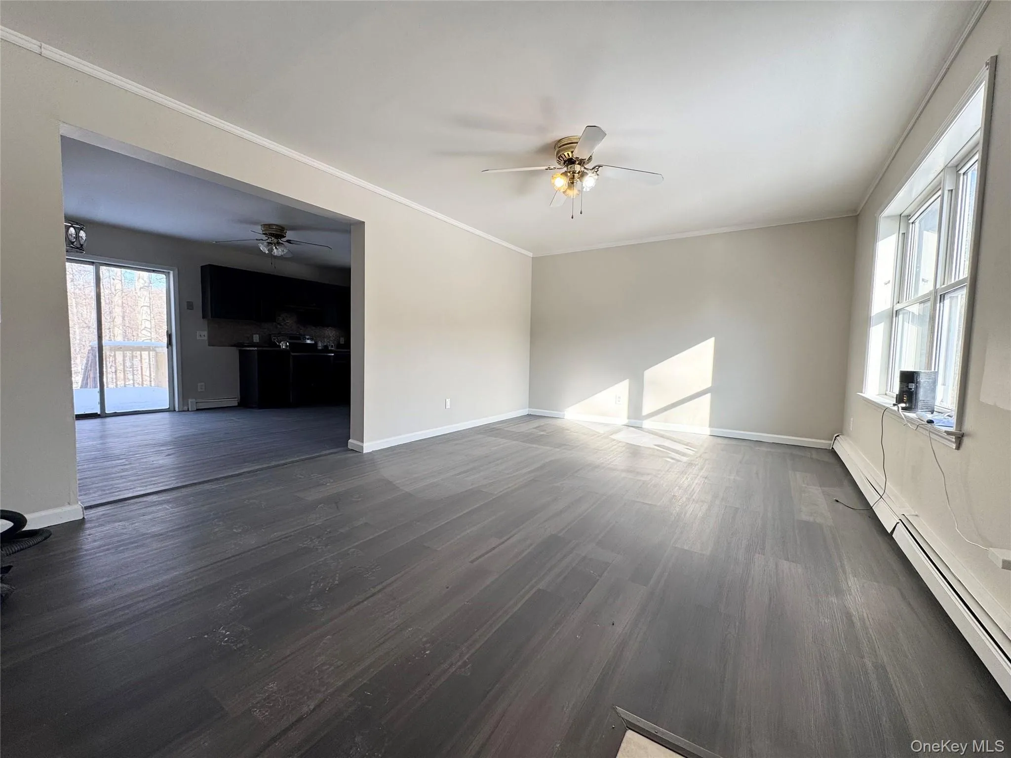 Unfurnished living room with a baseboard heating unit, dark wood-style flooring, ornamental molding, and ceiling fan Unfurnished living room with a baseboard heating unit, dark wood-style flooring, ornamental molding, and ceiling fan
