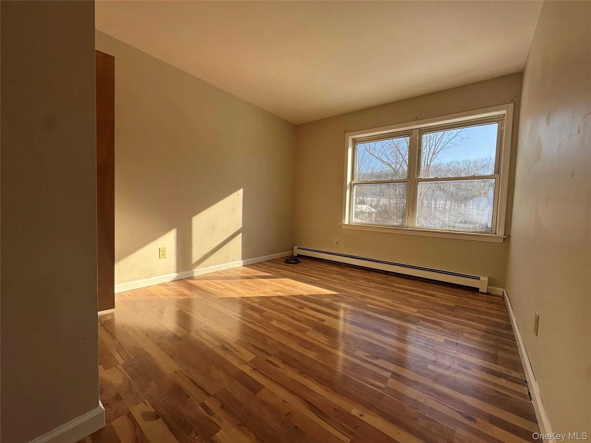 Spare room featuring wood finished floors and a baseboard radiator Spare room featuring wood finished floors and a baseboard radiator