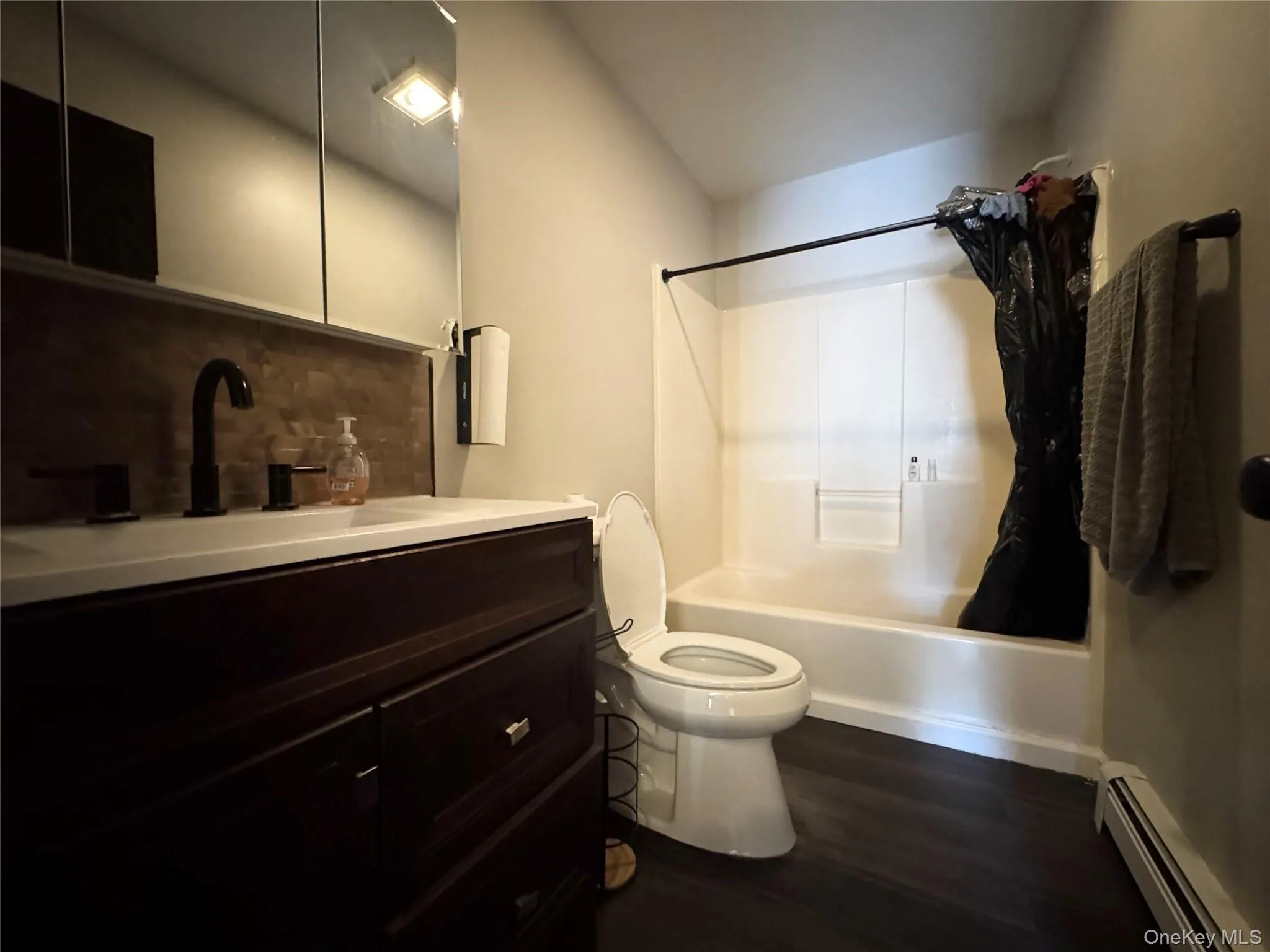 Full Bathroom with vanity, a baseboard heating unit, bathtub / shower combination, tasteful backsplash, and dark wood-style flooring Full Bathroom with vanity, a baseboard heating unit, bathtub / shower combination, tasteful backsplash, and dark wood-style flooring