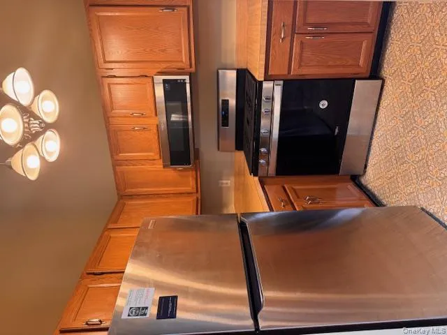 Kitchen with stainless steel appliances, light countertops, hanging light fixtures, and brown cabinetry Kitchen with stainless steel appliances, light countertops, hanging light fixtures, and brown cabinetry
