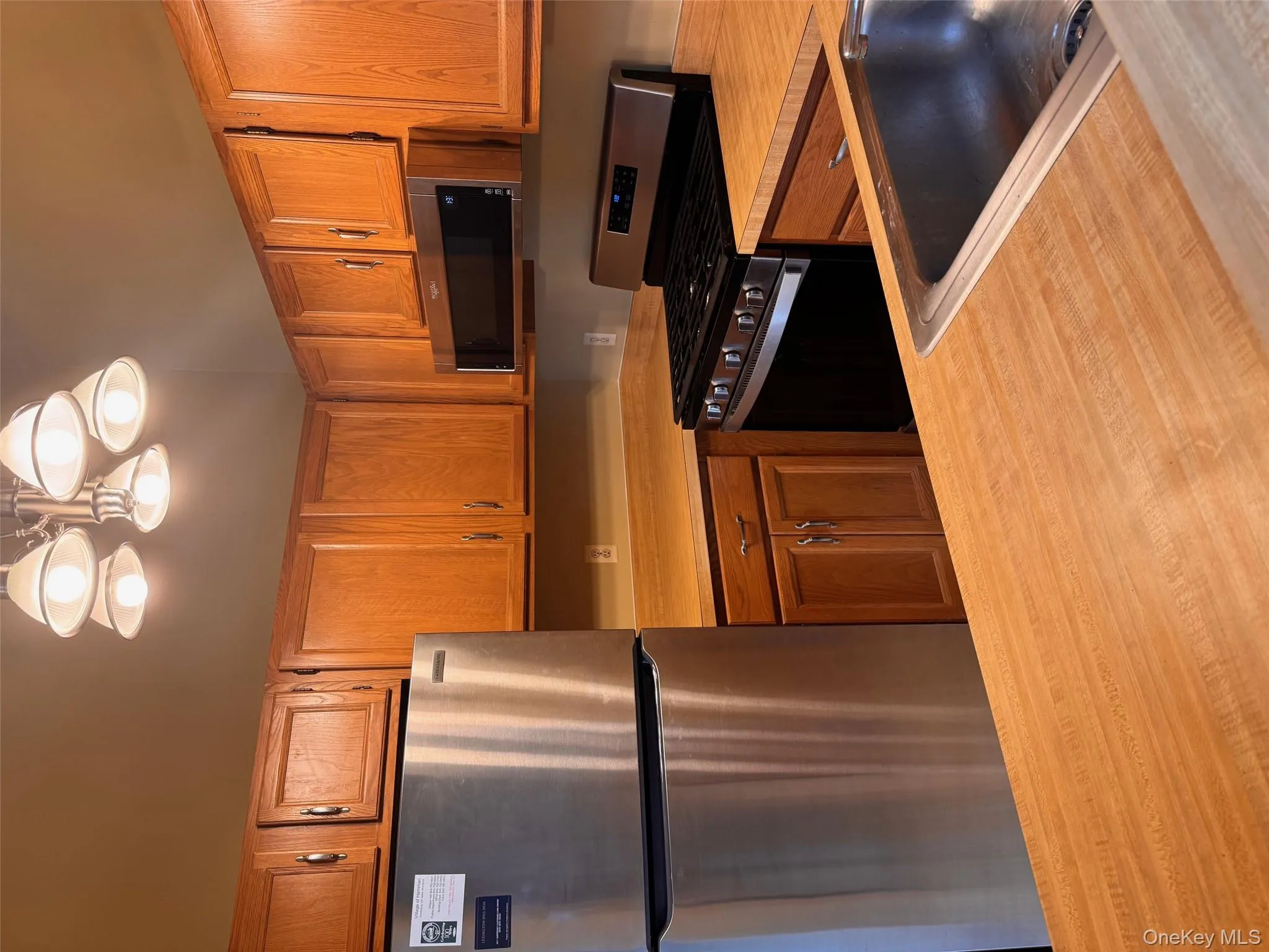 Kitchen with stainless steel appliances, light countertops, brown cabinets, hanging light fixtures, and a chandelier Kitchen with stainless steel appliances, light countertops, brown cabinets, hanging light fixtures, and a chandelier