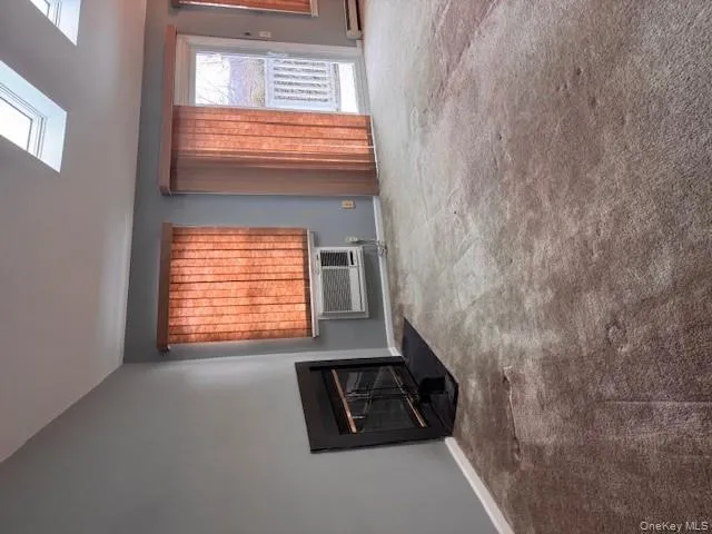 Unfurnished living room featuring carpet flooring, a fireplace with flush hearth, a skylight, and a baseboard heating unit Unfurnished living room featuring carpet flooring, a fireplace with flush hearth, a skylight, and a baseboard heating unit