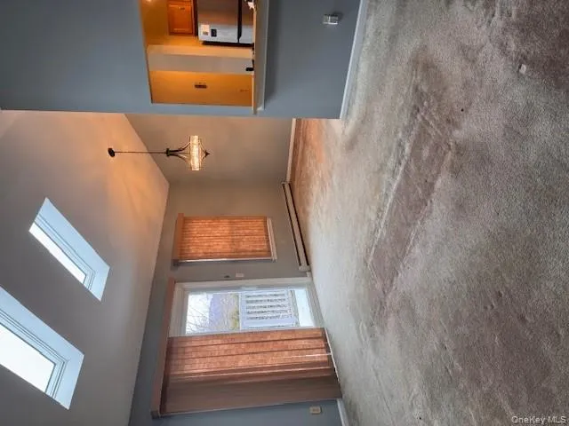 Unfurnished living room with vaulted ceiling, light colored carpet, baseboard heating, and a chandelier Unfurnished living room with vaulted ceiling, light colored carpet, baseboard heating, and a chandelier