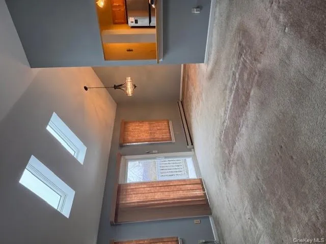 Unfurnished living room featuring light colored carpet, lofted ceiling, a baseboard heating unit, a chandelier, and a skylight Unfurnished living room featuring light colored carpet, lofted ceiling, a baseboard heating unit, a chandelier, and a skylight