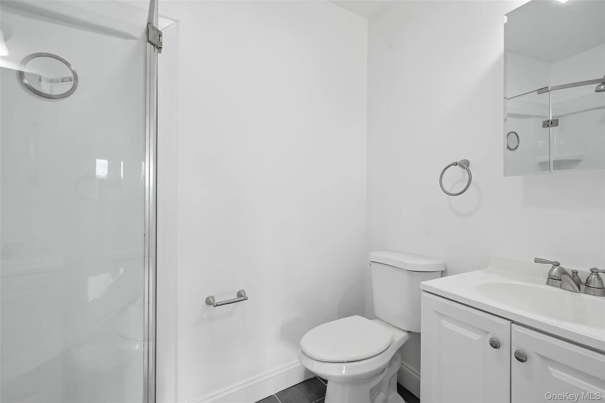 Full bath featuring a shower with shower door, vanity, and dark tile patterned flooring Full bath featuring a shower with shower door, vanity, and dark tile patterned flooring