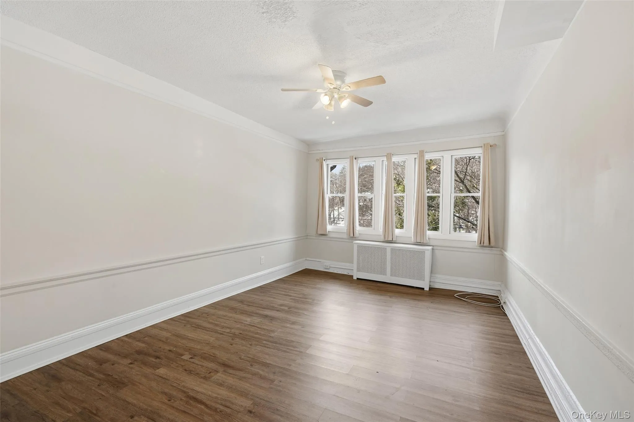 Unfurnished room featuring radiator, wood finished floors, a ceiling fan, and a textured ceiling Unfurnished room featuring radiator, wood finished floors, a ceiling fan, and a textured ceiling