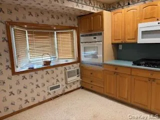 Kitchen with white microwave, light countertops, oven, wallpapered walls, and black gas stovetop Kitchen with white microwave, light countertops, oven, wallpapered walls, and black gas stovetop