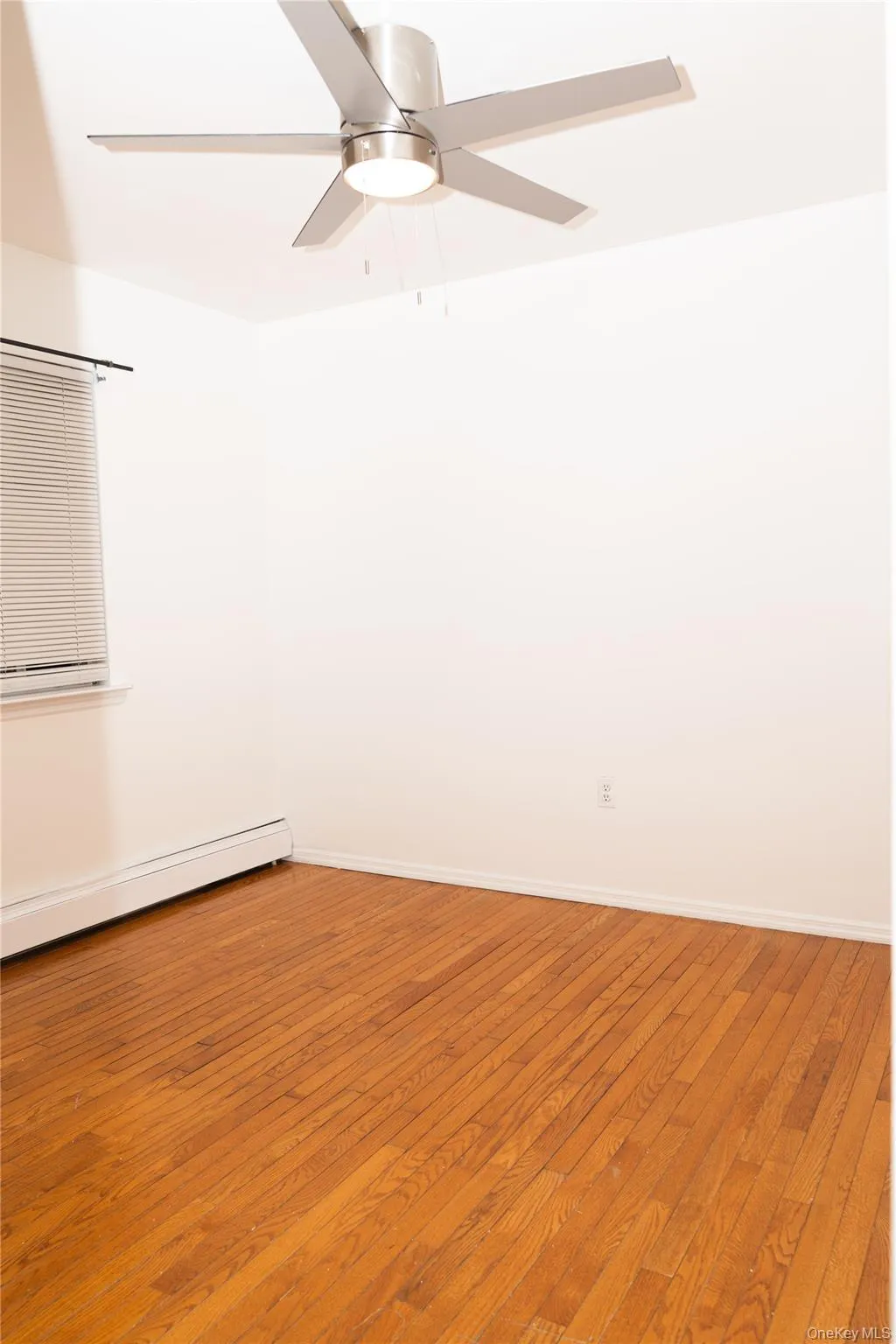 Unfurnished room featuring wood-type flooring, a baseboard heating unit, and a ceiling fan Unfurnished room featuring wood-type flooring, a baseboard heating unit, and a ceiling fan