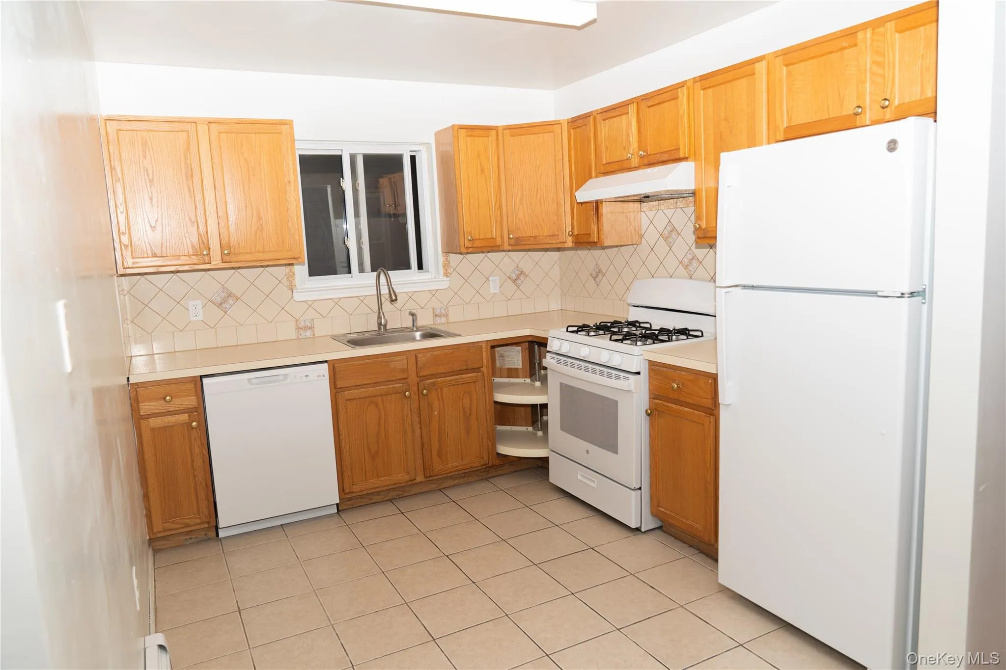 Kitchen with white appliances, light countertops, under cabinet range hood, and backsplash Kitchen with white appliances, light countertops, under cabinet range hood, and backsplash