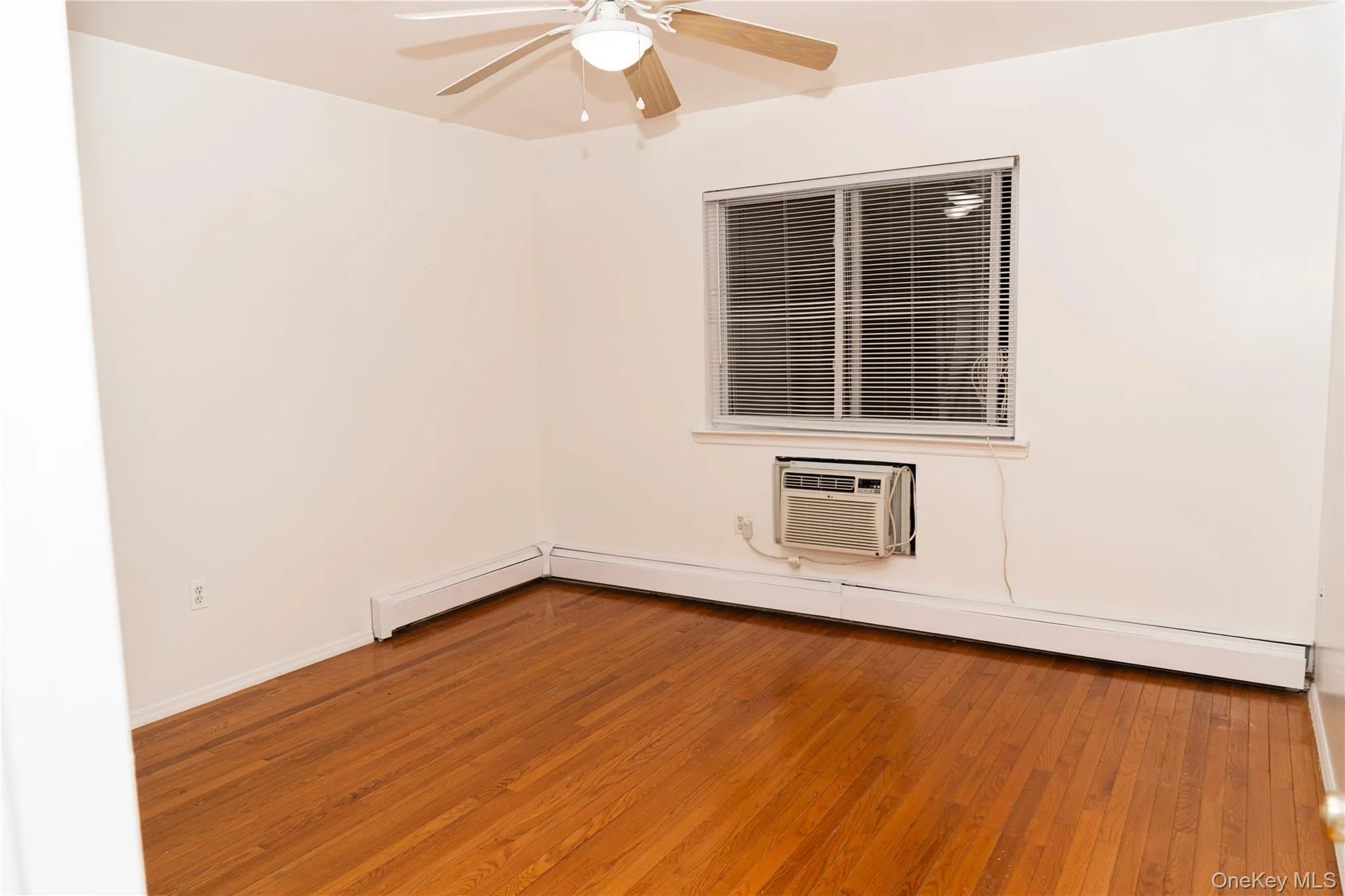 Spare room featuring hardwood / wood-style flooring, a baseboard heating unit, and a wall unit AC Spare room featuring hardwood / wood-style flooring, a baseboard heating unit, and a wall unit AC