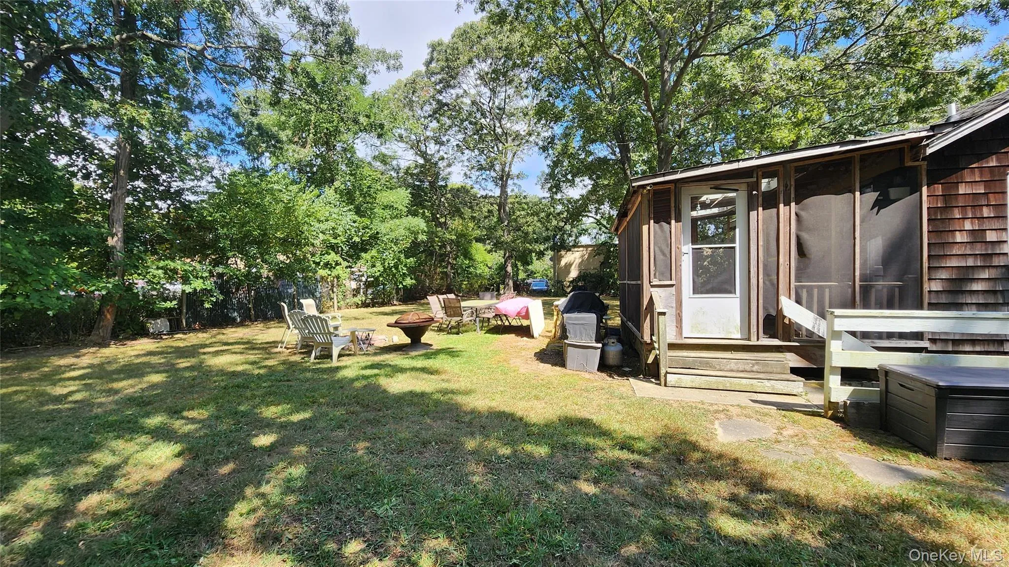 View of green lawn featuring a sunroom, a fire pit, view of wooded area, and entry steps View of green lawn featuring a sunroom, a fire pit, view of wooded area, and entry steps