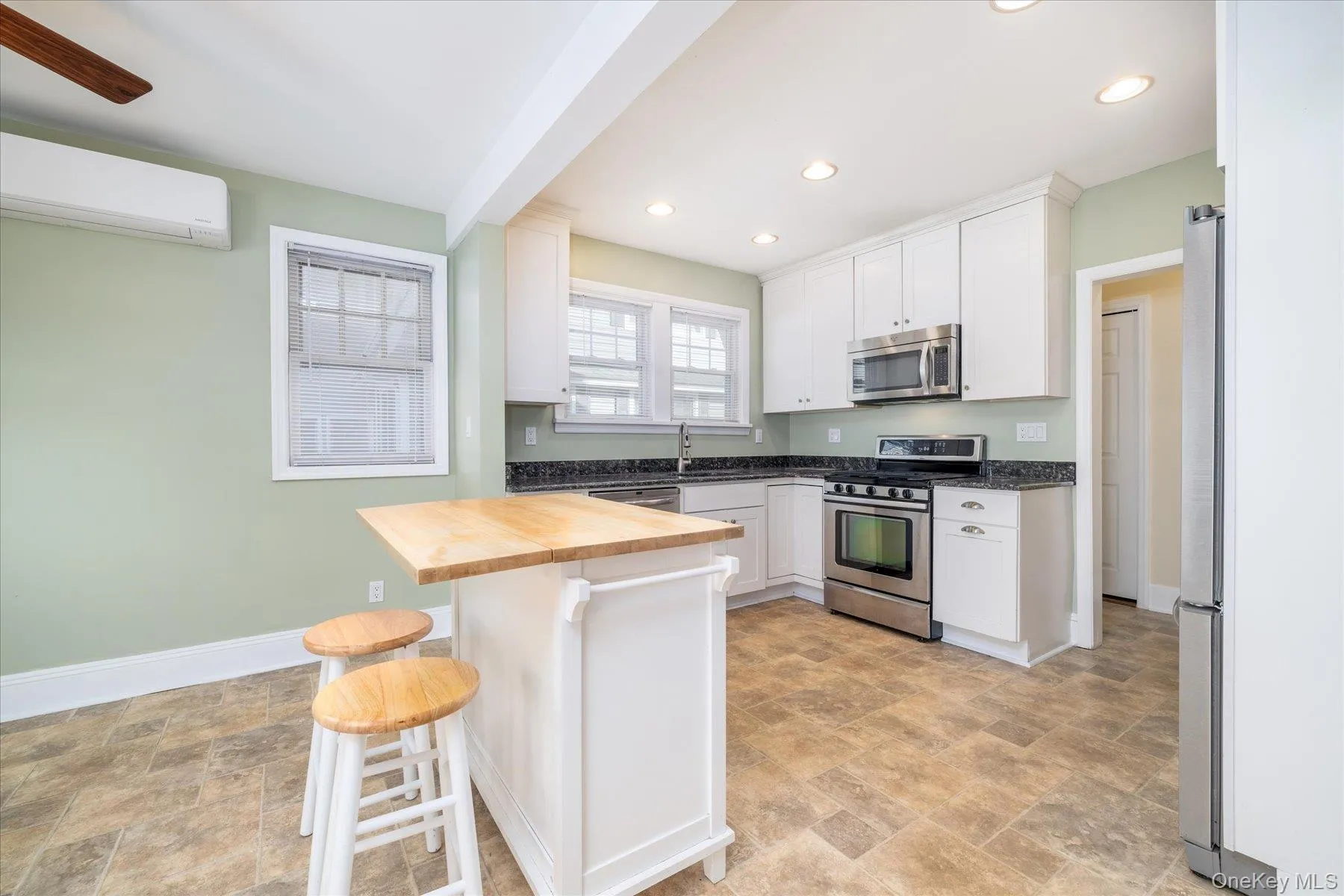 Kitchen featuring butcher block countertops, stone finish flooring, stainless steel appliances, a kitchen breakfast bar, and white cabinetry Kitchen featuring butcher block countertops, stone finish flooring, stainless steel appliances, a kitchen breakfast bar, and white cabinetry