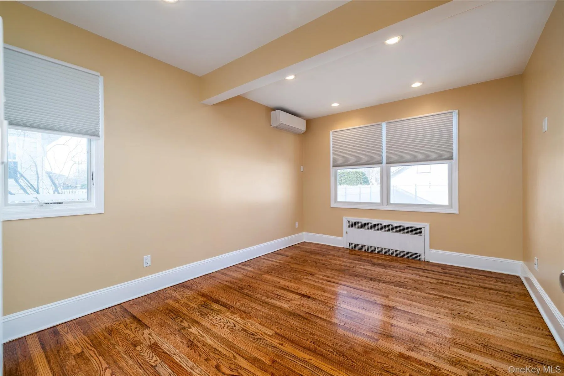Empty room featuring recessed lighting, radiator, wood finished floors, and an AC wall unit Empty room featuring recessed lighting, radiator, wood finished floors, and an AC wall unit