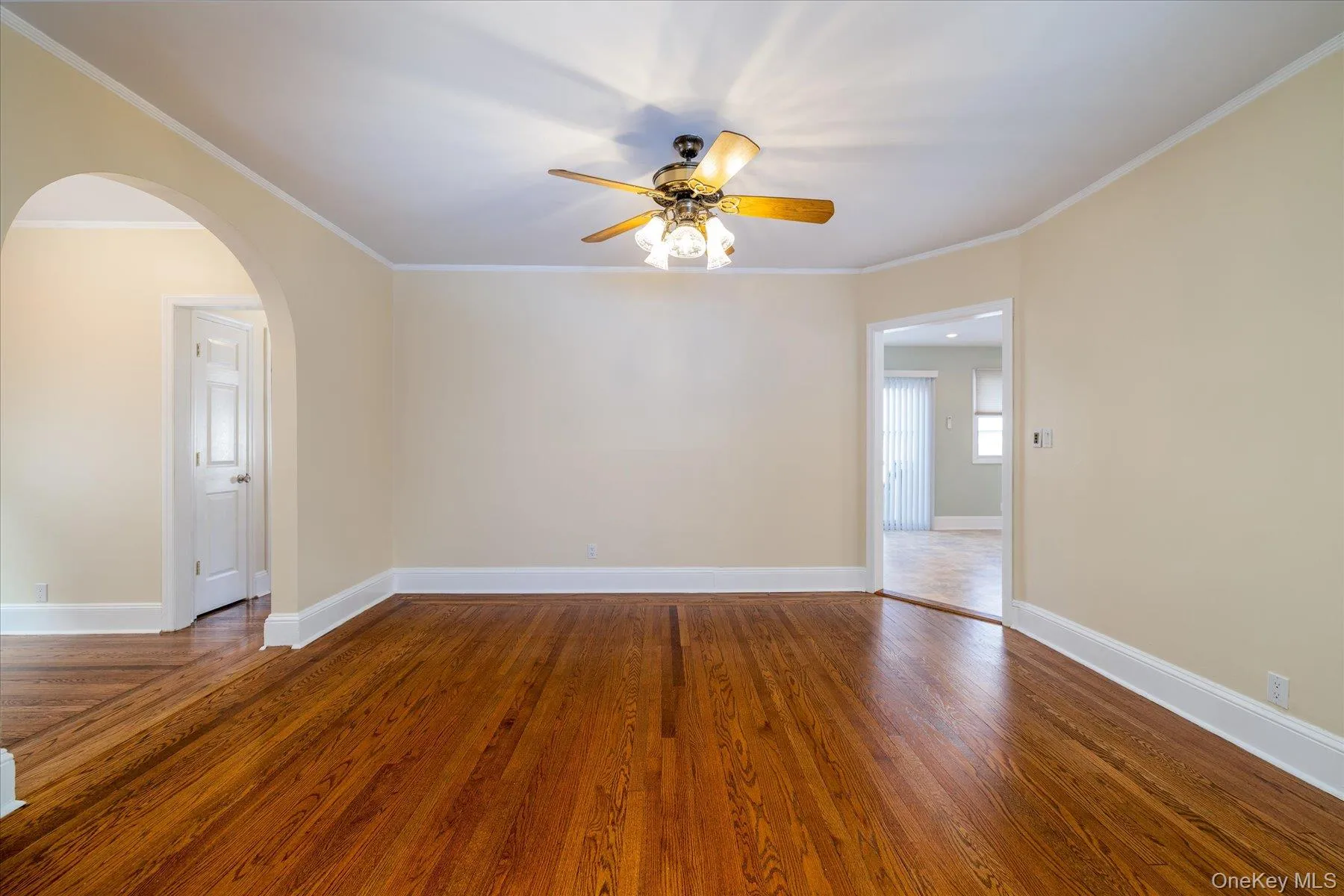 Empty room with crown molding, dark wood-type flooring, arched walkways, and a ceiling fan Empty room with crown molding, dark wood-type flooring, arched walkways, and a ceiling fan
