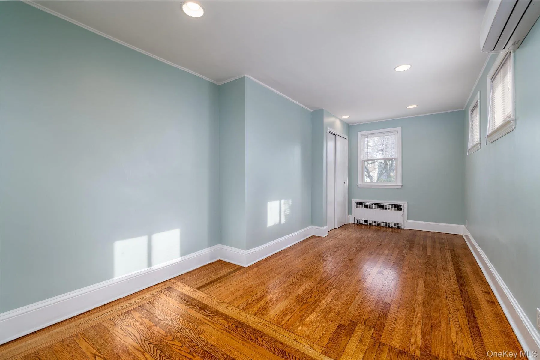 Unfurnished room featuring hardwood / wood-style floors, a wall mounted air conditioner, recessed lighting, radiator heating unit, and ornamental molding Unfurnished room featuring hardwood / wood-style floors, a wall mounted air conditioner, recessed lighting, radiator heating unit, and ornamental molding