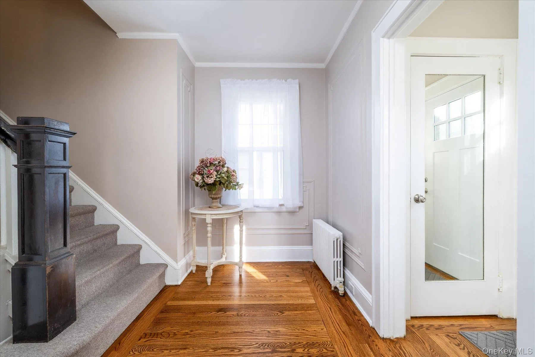 Foyer entrance featuring radiator, stairs, wood finished floors, and ornamental molding Foyer entrance featuring radiator, stairs, wood finished floors, and ornamental molding