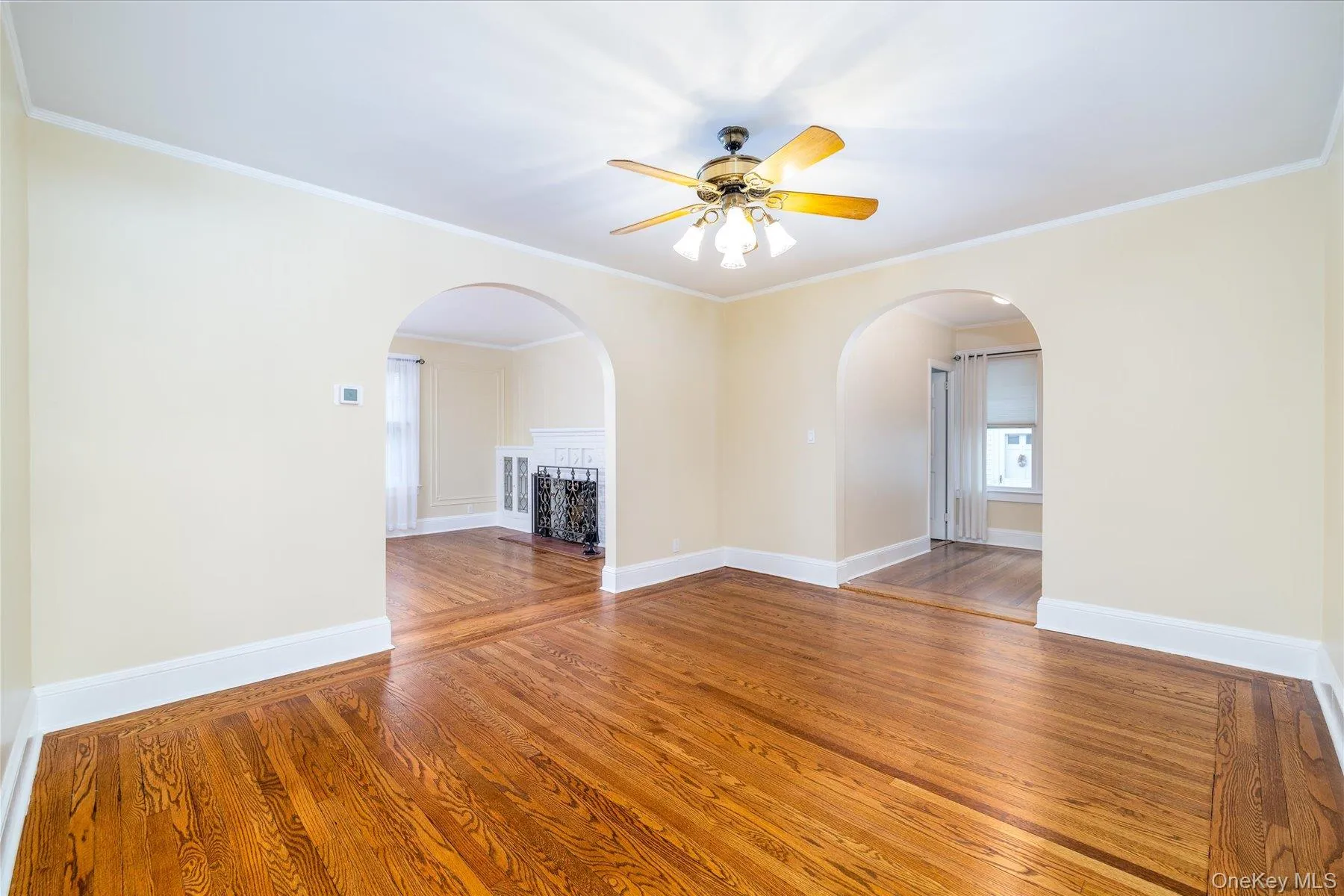 Unfurnished room featuring hardwood / wood-style floors, arched walkways, crown molding, and a ceiling fan Unfurnished room featuring hardwood / wood-style floors, arched walkways, crown molding, and a ceiling fan