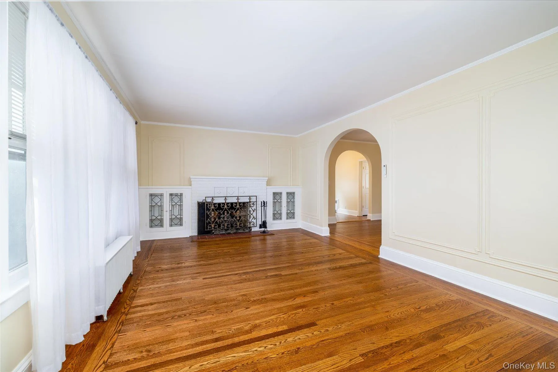 Unfurnished living room with a decorative wall, arched walkways, wood finished floors, radiator heating unit, and crown molding Unfurnished living room with a decorative wall, arched walkways, wood finished floors, radiator heating unit, and crown molding