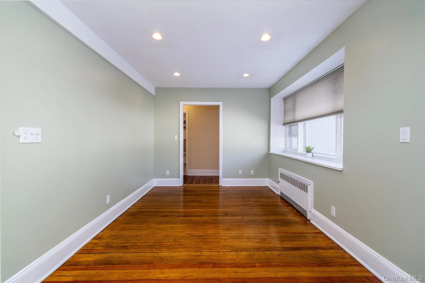 Spare room with radiator heating unit, dark wood-style floors, and recessed lighting Spare room with radiator heating unit, dark wood-style floors, and recessed lighting