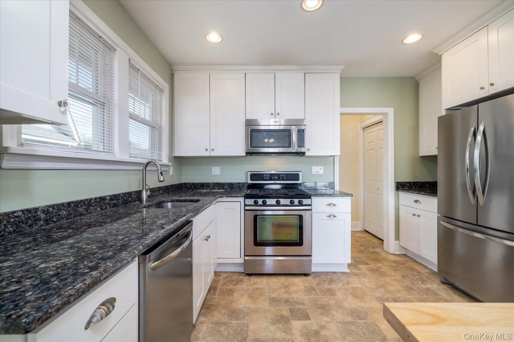 Kitchen featuring appliances with stainless steel finishes, dark stone counters, stone finish floors, white cabinetry, and recessed lighting Kitchen featuring appliances with stainless steel finishes, dark stone counters, stone finish floors, white cabinetry, and recessed lighting