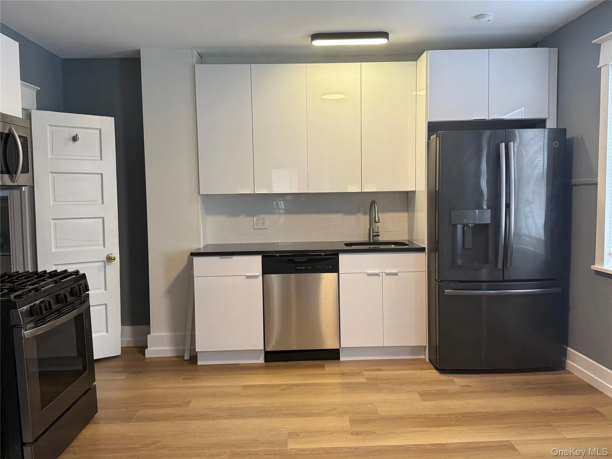 Kitchen with appliances with stainless steel finishes, tasteful backsplash, white cabinetry, and light wood-type flooring Kitchen with appliances with stainless steel finishes, tasteful backsplash, white cabinetry, and light wood-type flooring