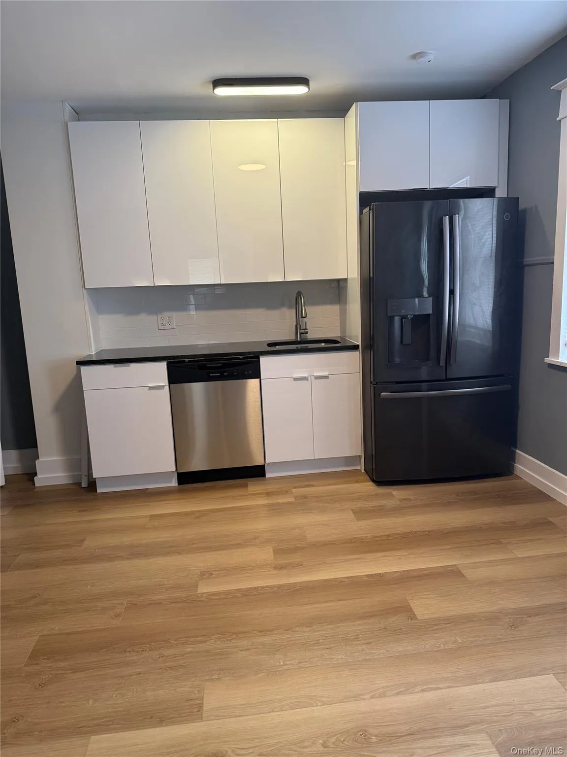 Kitchen with black refrigerator with ice dispenser, white cabinets, modern cabinets, dishwasher, and light wood-style flooring Kitchen with black refrigerator with ice dispenser, white cabinets, modern cabinets, dishwasher, and light wood-style flooring