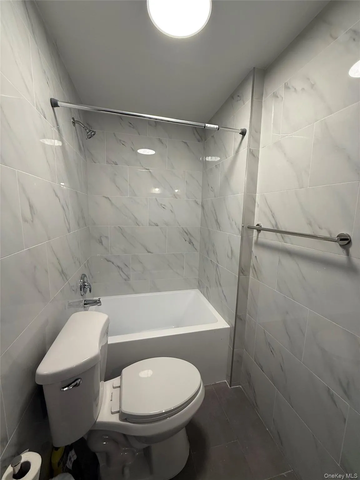 Bathroom featuring tile walls, shower / bath combination, and dark tile patterned flooring Bathroom featuring tile walls, shower / bath combination, and dark tile patterned flooring