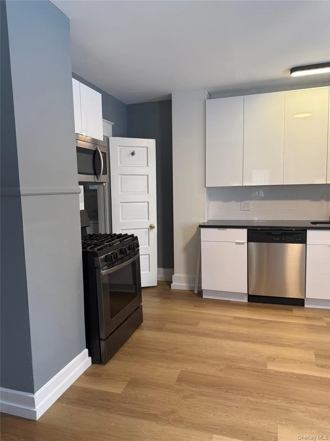 Kitchen with appliances with stainless steel finishes, white cabinetry, dark countertops, light wood-style floors, and modern cabinets Kitchen with appliances with stainless steel finishes, white cabinetry, dark countertops, light wood-style floors, and modern cabinets