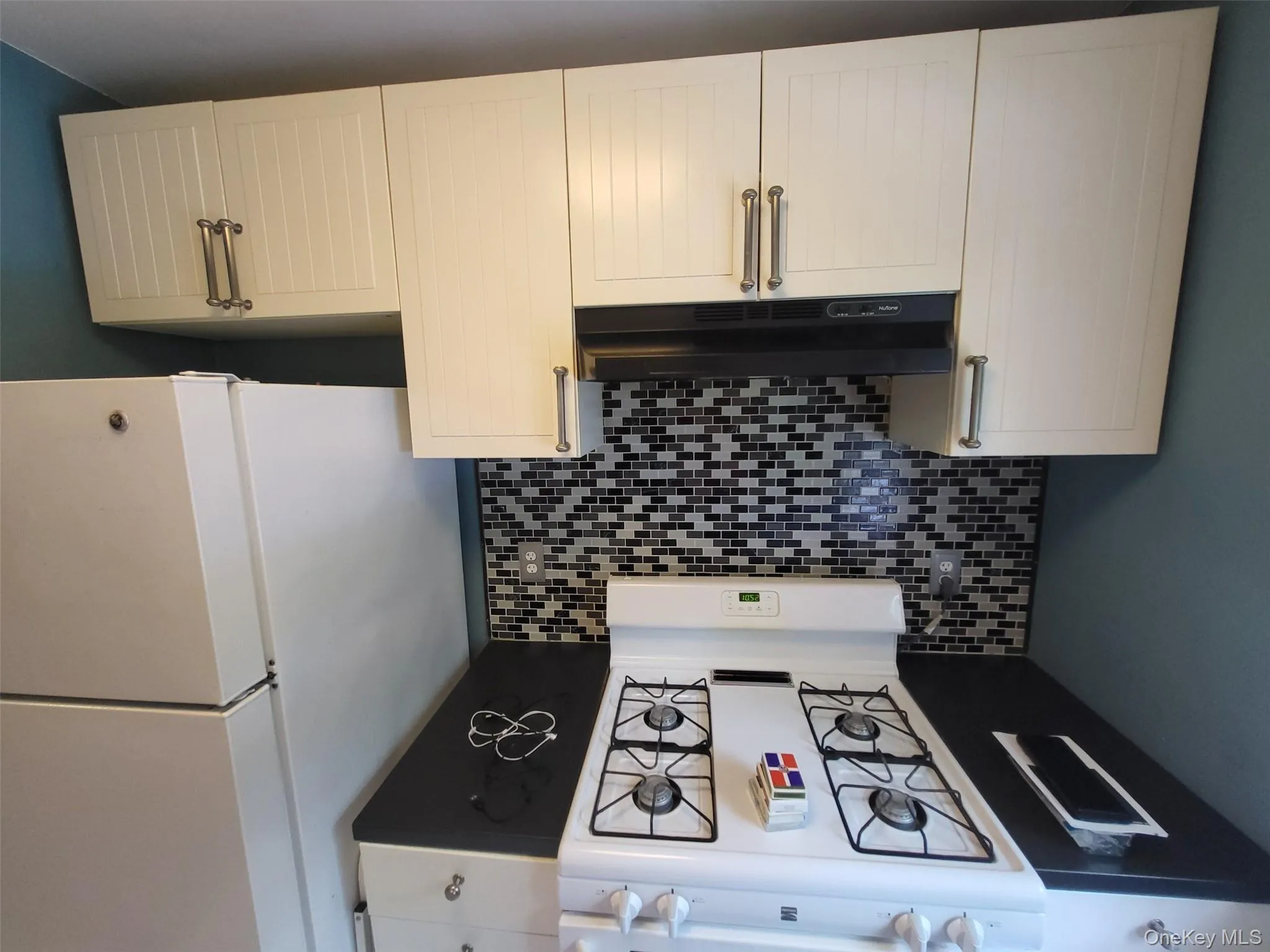 Kitchen featuring white appliances, under cabinet range hood, and decorative backsplash Kitchen featuring white appliances, under cabinet range hood, and decorative backsplash
