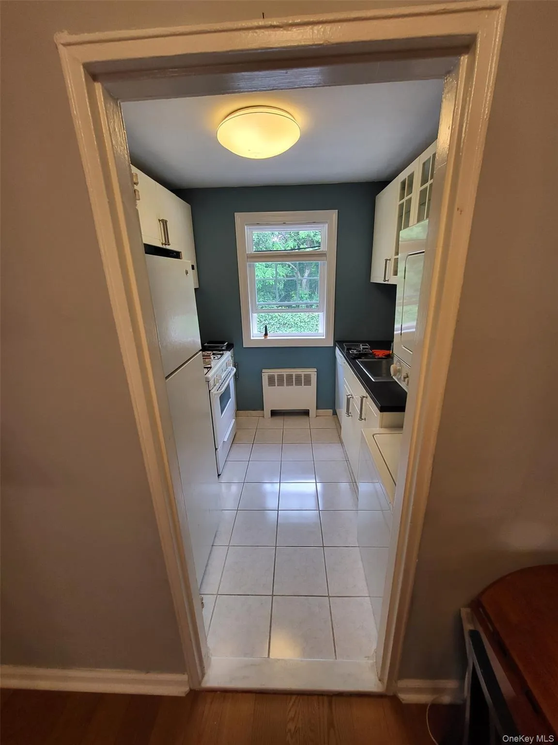 Kitchen with radiator heating unit, dark countertops, white cabinetry, and white appliances Kitchen with radiator heating unit, dark countertops, white cabinetry, and white appliances