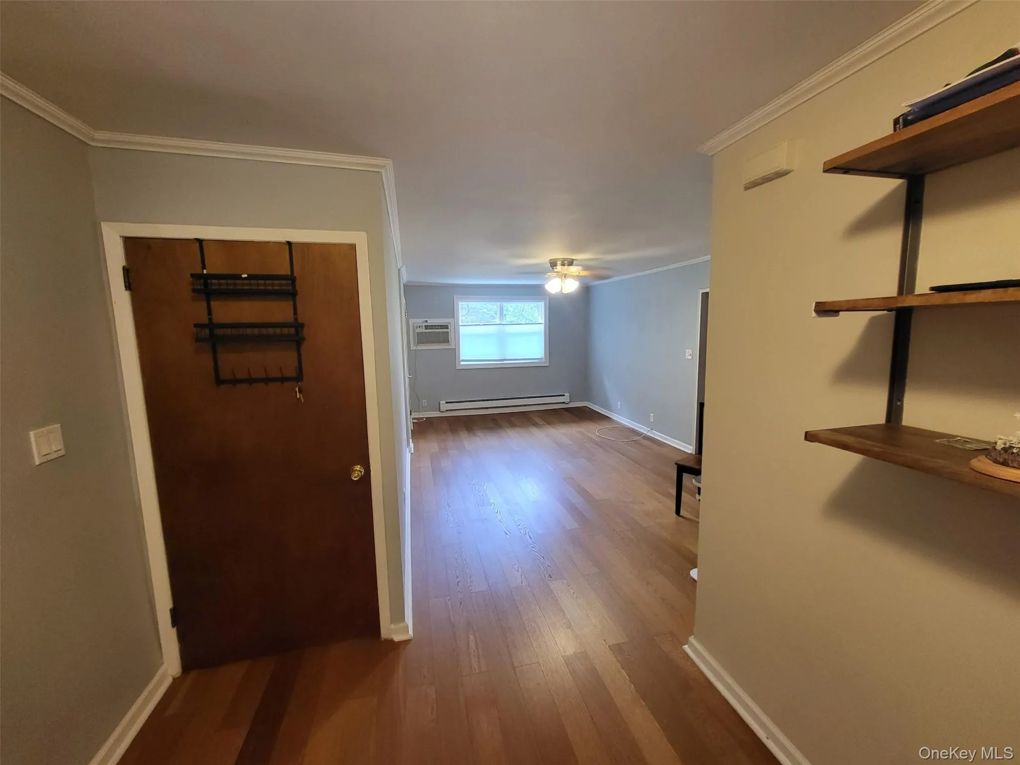 Hallway featuring dark wood finished floors, baseboard heating, ornamental molding, and a wall unit AC Hallway featuring dark wood finished floors, baseboard heating, ornamental molding, and a wall unit AC