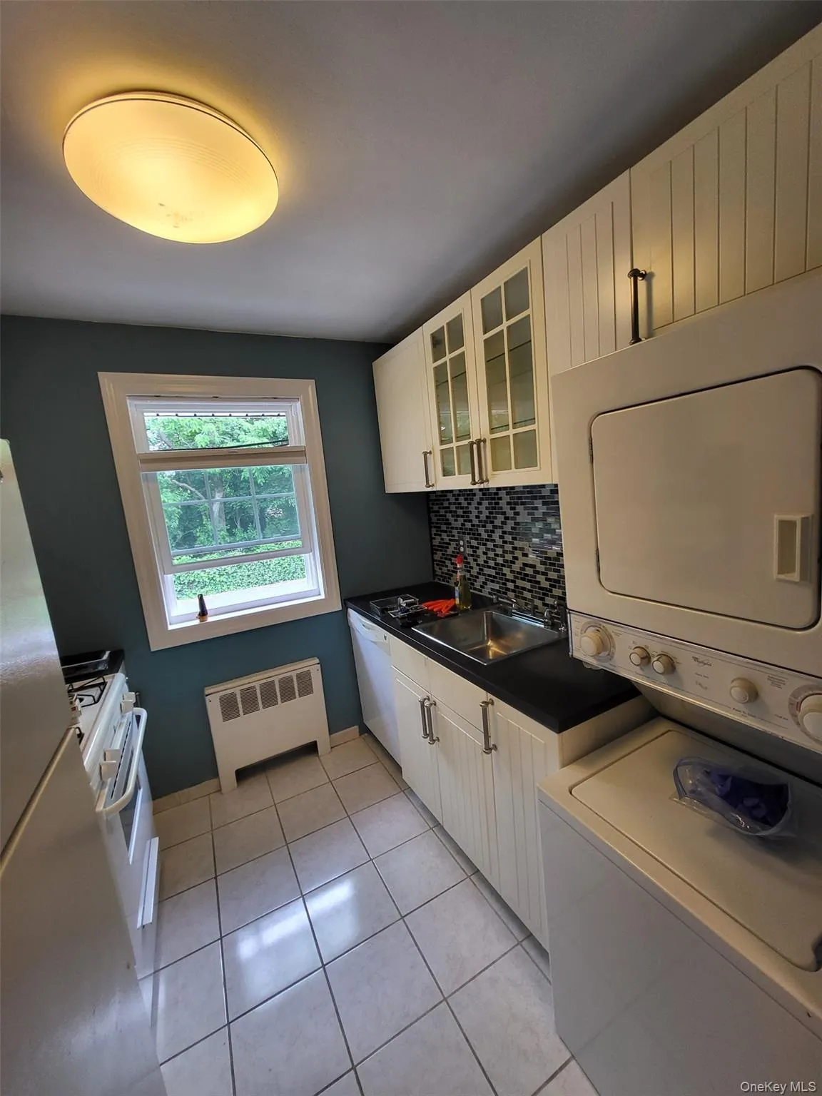 Laundry room featuring radiator, stacked washer and clothes dryer, and light tile patterned floors Laundry room featuring radiator, stacked washer and clothes dryer, and light tile patterned floors