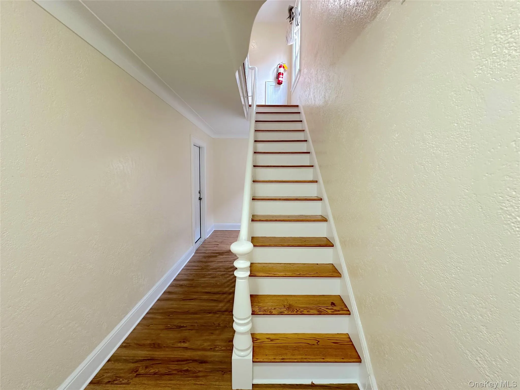 Staircase featuring a textured wall, wood finished floors, and crown molding Staircase featuring a textured wall, wood finished floors, and crown molding