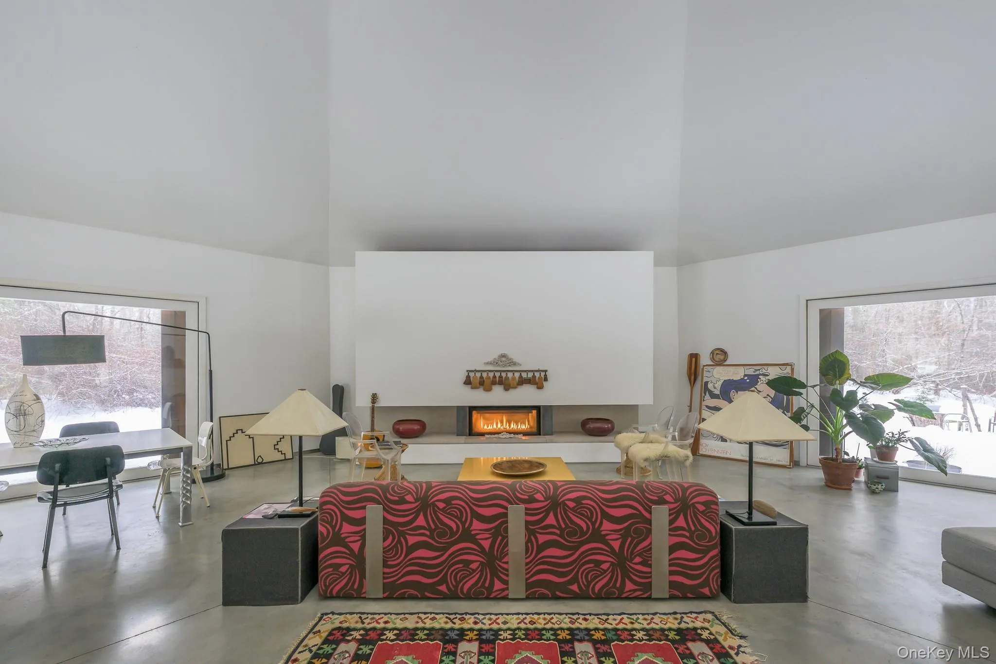 Living area with a high ceiling, healthy amount of natural light, finished concrete flooring, and a lit fireplace Living area with a high ceiling, healthy amount of natural light, finished concrete flooring, and a lit fireplace