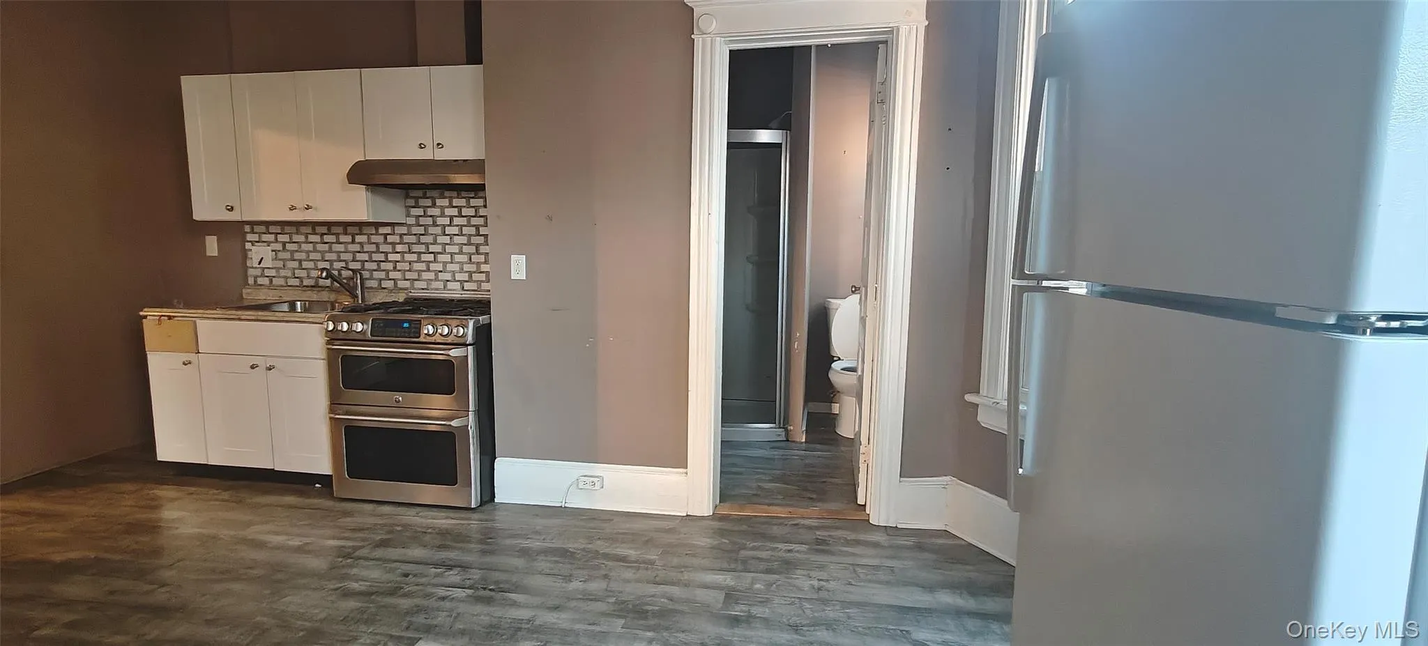 Kitchen featuring appliances with stainless steel finishes, white cabinetry, backsplash, under cabinet range hood, and light countertops Kitchen featuring appliances with stainless steel finishes, white cabinetry, backsplash, under cabinet range hood, and light countertops