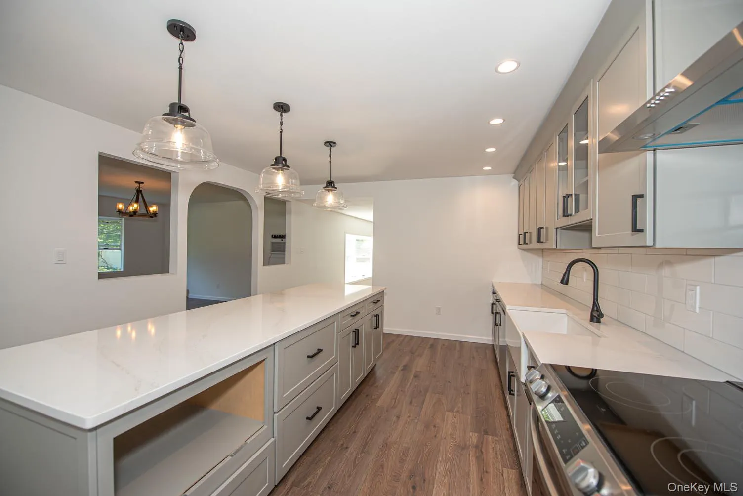 Kitchen with gray cabinets, stainless steel range with electric stovetop, wall chimney range hood, decorative light fixtures, and recessed lighting Kitchen with gray cabinets, stainless steel range with electric stovetop, wall chimney range hood, decorative light fixtures, and recessed lighting