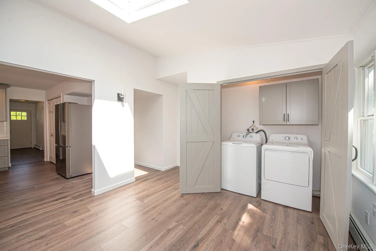Washroom with baseboard heating, light wood finished floors, washer and dryer, and a skylight Washroom with baseboard heating, light wood finished floors, washer and dryer, and a skylight